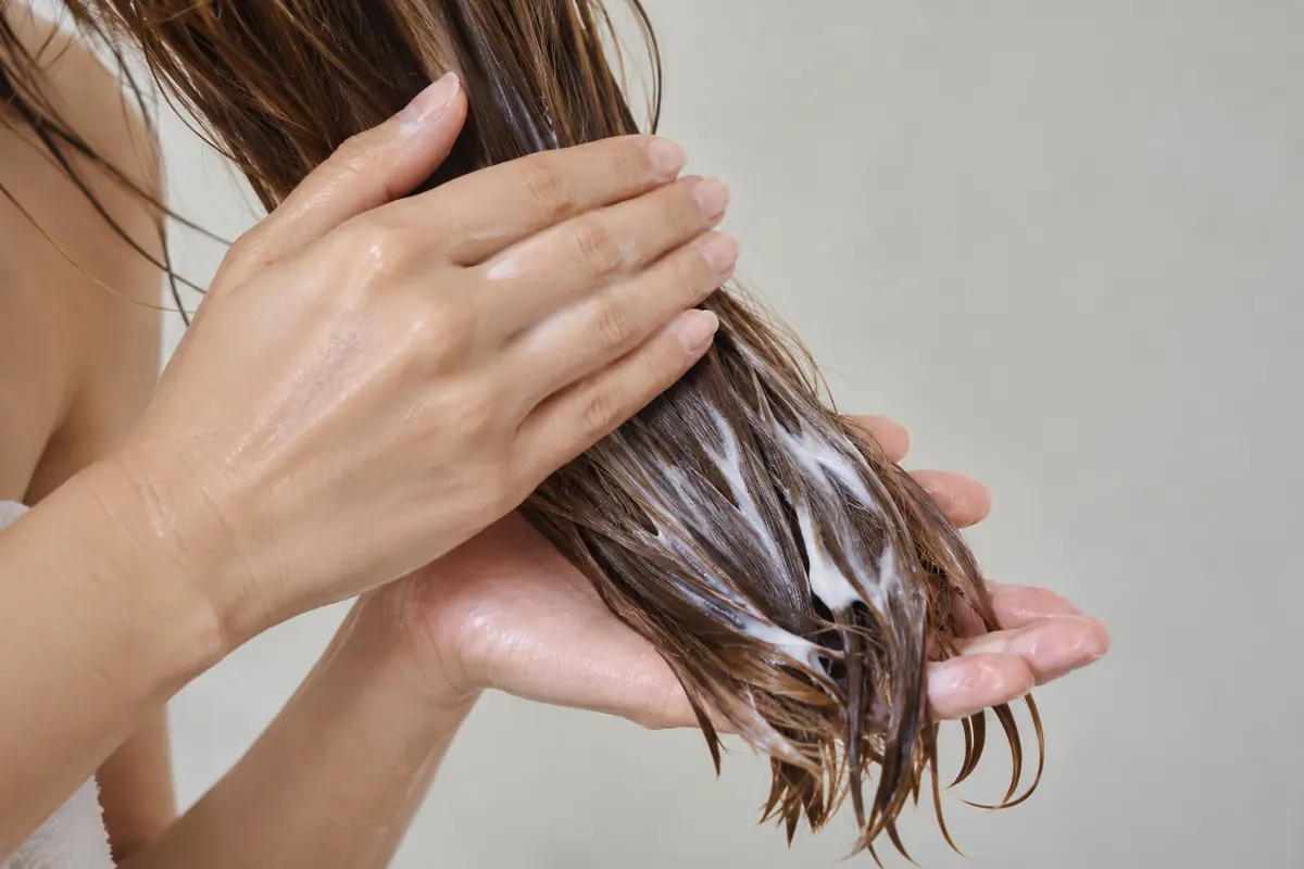 Hands spreading conditioner through hair lengths